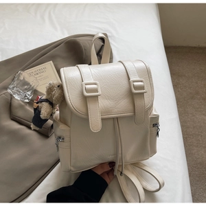 Détail du sac à dos en similicuir crème avec texture veinée et breloque ours
