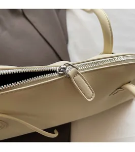 Detail shot of a silver metal zipper and hardware puller on a beige leather bag
