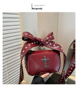 Macro detail of wine red leather bag with silver rivets and metal cross pendant