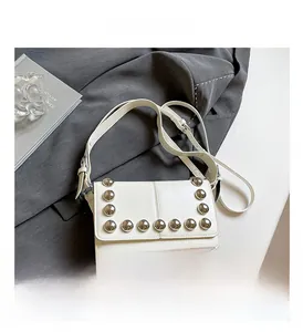 Close-up of white leather handbag featuring silver stud rivets and adjustable strap detail