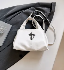 Dettaglio della borsa in pelle litchi bianca con croce gotica in metallo e catena