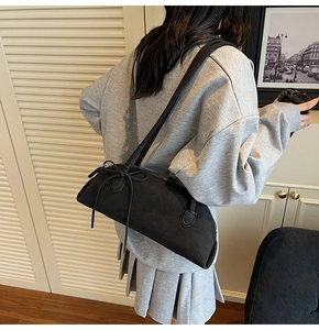 Detailed side view of a black baguette shoulder bag with a ribbon bow on grainy leather