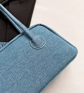 Macro detail of grey-blue denim shoulder bag showing reinforced stitching and twill fabric