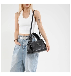 Detail of black leather bag with silver gothic cross and rivet texture on model