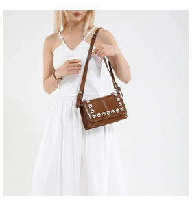 Detail of dark brown leather crossbody bag featuring silver rivets on a white dress