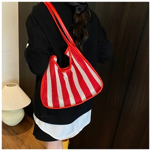 Detail of a red and white striped mesh tote bag with leather handles on female shoulder