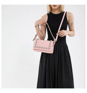 Detail of pink PU leather crossbody bag with silver rivet studs on a black dress model
