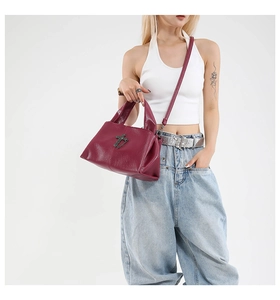 Detail of burgundy pebbled leather tote bag with dark gray metal cross and shoulder strap