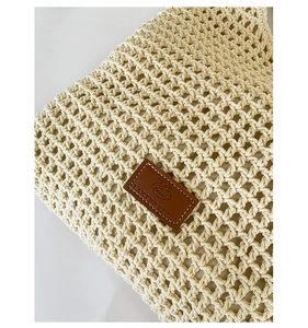 Close-up of beige woven hollow handbag featuring a brown leather label with stitch detail
