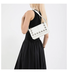 Close-up of a white leather shoulder bag featuring decorative silver metal studs on edges