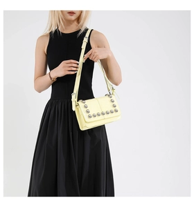 Detailed view of a light yellow biker crossbody bag featuring silver metal rivets