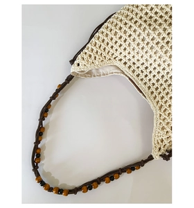 Detail of woven straw tote with dark brown wooden bead accents and bohemian texture