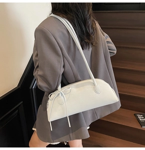 White shell-shaped shoulder bag with bow detail shown on a model in a street style setting