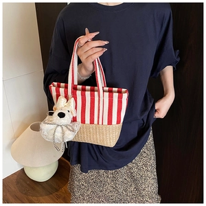 Detail of red striped canvas and woven straw bucket bag with a plush dog charm