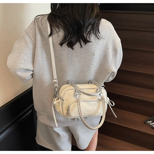 Close-up of a cream crossbody bowling bag with silver metallic trim on a person