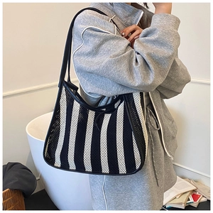 Detail of striped mesh shoulder bag with leather piping on a model in a cozy indoor setting