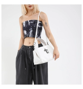 Detail of white glossy tote bag featuring a black metal cross pendant and chain charm