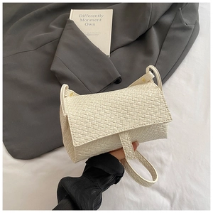 Detail shot of the woven leather texture and flap design on a white minimalist shoulder bag