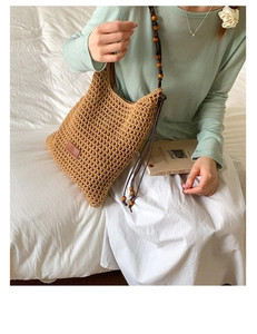 Detail of woven straw tote bag featuring decorative wooden beads and slim shoulder straps