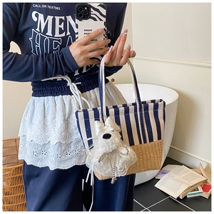 Detail of striped beach tote with straw base and cute plush puppy charm accessory