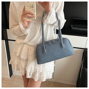 Detail of blue denim shoulder bag showing white contrast stitching and dual zipper closure