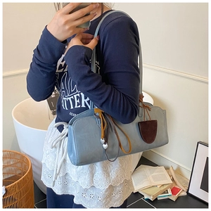 Sac baguette chic en cuir bleu Morandi avec pendentif cœur porté par un mannequin