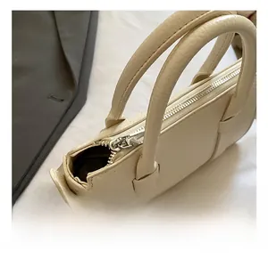 Close-up of cream textured leather handbag featuring silver metal zipper and dual handles