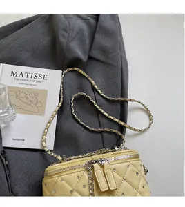 Detail of yellow quilted box bag with silver studs and chain on grey fabric