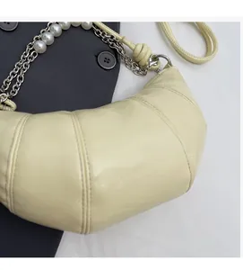 Close-up of yellow crescent bag with pleated leather, pearl chain, and metal strap detail