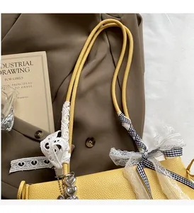 Detail der gelben Lederhandtasche mit Spitzenschleife und Herzanhänger aus Silber