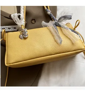 Detailaufnahme der gelben Baguette-Tasche mit Spitze, Karoschleife und Herzanhänger