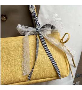 Detail einer gelben Ledertasche mit Schleife aus Spitze und kariertem Banddekor