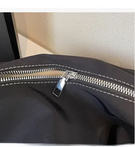 Close-up of smooth silver metal zipper and white decorative stitching on black fabric