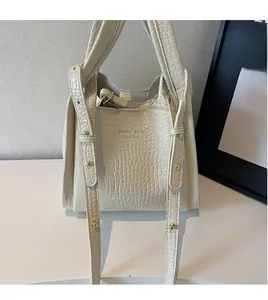 Detail of cream crocodile textured handbag with adjustable strap and gold rivets