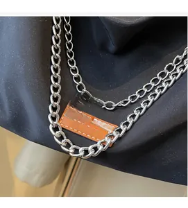 Close-up of black nylon tote bag featuring silver metal chains and brown leather patch