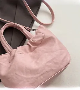 Detailed shot of pink pleated handbag showing soft texture and handle on a dark grey suit