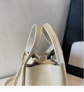 Detail of cream bucket bag with crocodile texture and gold logo on front side