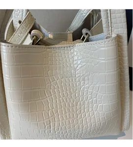 Detailed close-up of cream crocodile pattern leather handbag with gold metal hardware