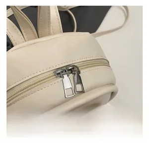 Close-up of dual silver metal zippers and PU leather texture on cream mini backpack