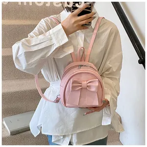 Model wearing a mini light pink PU leather backpack with a decorative bow on stairs