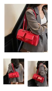 Detail of red glossy cylinder handbag with dual front pockets and leather shoulder strap