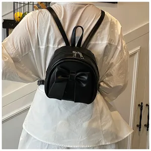 Rear view of a black mini backpack featuring a large bow and adjustable straps on a model