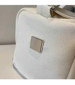 Macro shot of white lychee grain leather handbag with minimalist silver metal square plaque