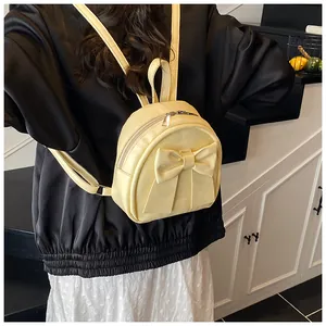 Cream yellow mini backpack with oversized bow detail shown on a model's back