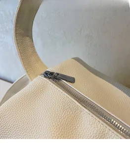 Close-up of smooth silver zipper and pebbled leather texture on cream crossbody bag