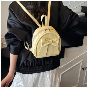 Rear view of a yellow mini backpack with a large bow detail on a fashion model