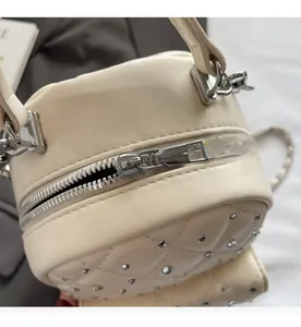 Close-up of smooth silver zipper and quilted rhinestone detail on a cream shoulder bag