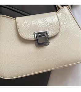 Détail du fermoir métallique carré sur sac à bandoulière blanc crème en cuir plissé