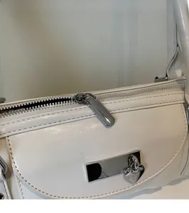Detail of silver heart charm and zipper on white polished synthetic leather bag