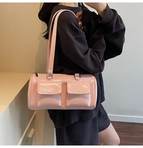 Detailed view of a pink glossy patent leather cylindrical shoulder bag with front flap pockets